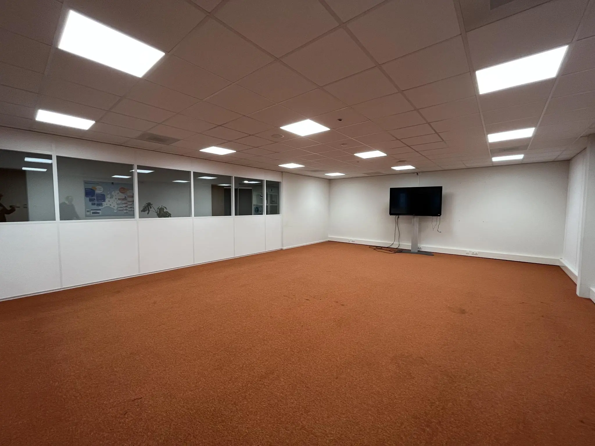 Leeg vergader- of kantoorruimte aan de Niels Bohrweg met oranje vloerbedekking, witte wanden en een scherm aan de muur.